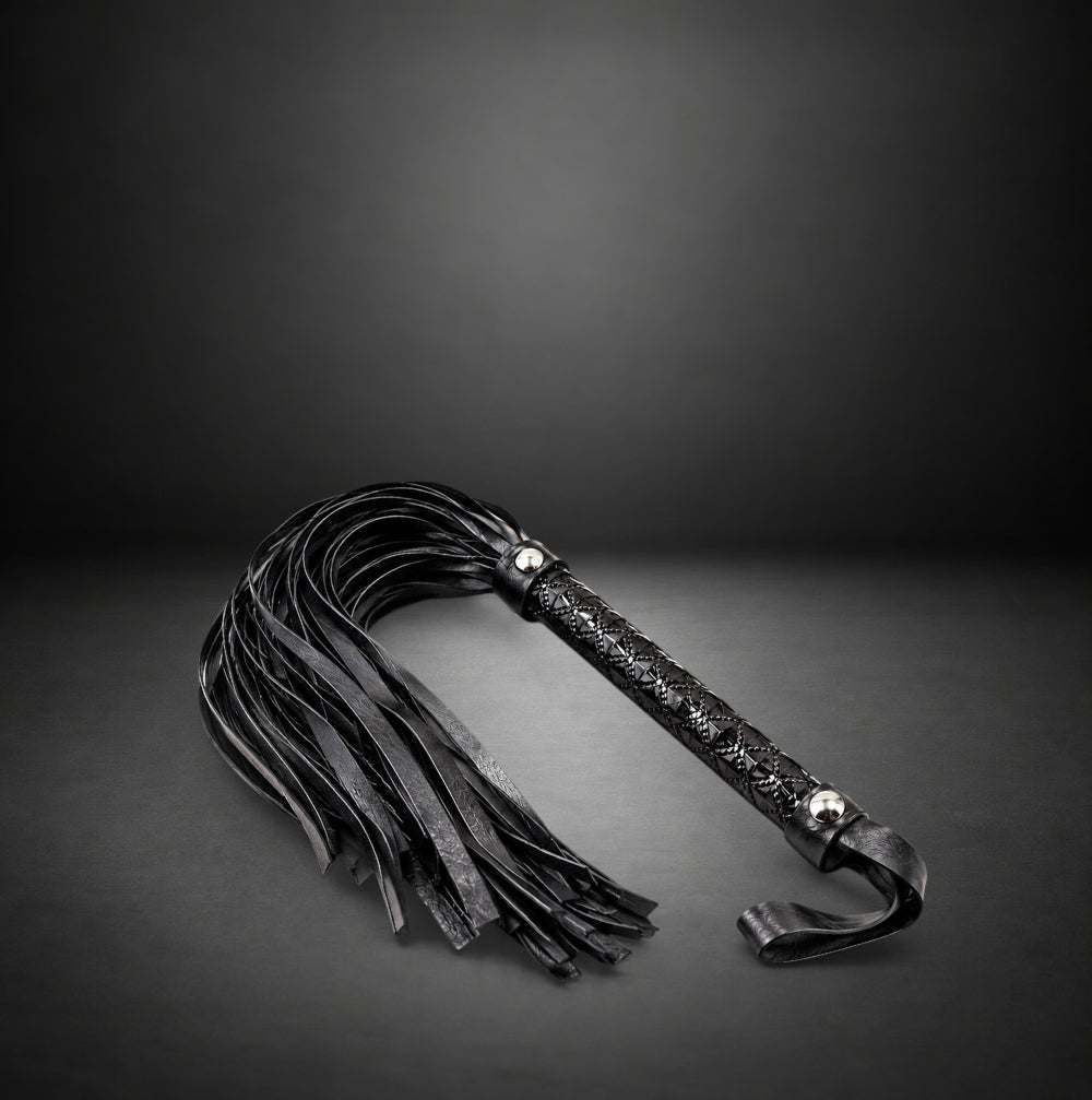 RealCock Toys black faux leather flogger with soft suede-style tails and textured diamond-pattern handle